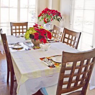 A dining table set with a white tablecloth and decorated with poinsettia flowers.