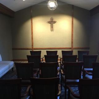 A small chapel interior with rows of chairs facing a wall-mounted cross.