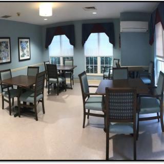 A cozy dining room with multiple tables and chairs arranged near large windows, featuring soft lighting and elegant decor.