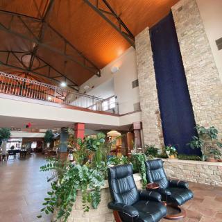 A spacious hotel lobby with a high ceiling, featuring a stone wall, water feature, plants, and comfortable seating.