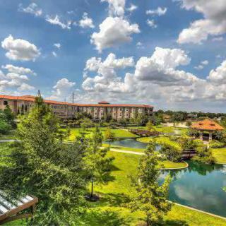 A beautiful landscape featuring a large building surrounded by lush greenery and serene ponds under a partly cloudy sky.