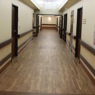 A long and wide corridor with doors on either side, featuring wooden flooring and overhead lighting.