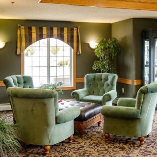 A cozy living room with green chairs arranged around a central coffee table, illuminated by natural light from a large window.