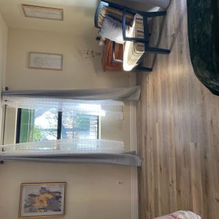 A cozy room with a wooden floor, featuring a small desk, a chair, and sheer curtains.