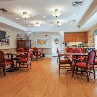 A spacious dining room with multiple tables and chairs, featuring a kitchen area in the background.