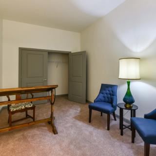 A cozy room with two blue chairs, a wooden table, and a green lamp beside an open closet.