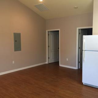An empty apartment interior featuring hardwood floors, a white refrigerator, and two doors.
