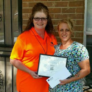 Two women proudly posing with a certificate and documents, celebrating an achievement.