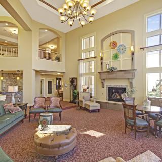 Elegant living room with a high ceiling, chandelier, and fireplace, featuring classic furniture and abundant natural light.