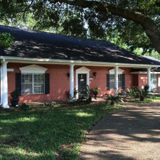 A suburban house with brick exterior and white columns, surrounded by trees and a well-maintained yard.