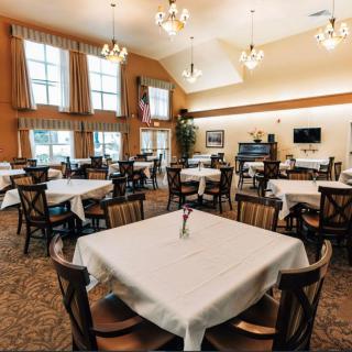 A spacious dining room with neatly arranged tables and chairs, featuring elegant chandeliers and large windows.