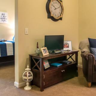 A cozy living room corner with a TV stand, decorative items, and a glimpse into a bedroom.