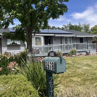 A suburban house with solar panels and a mailbox in the front yard on a sunny day.