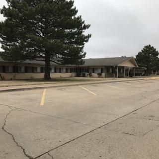 A spacious commercial building with an empty parking lot, framed by trees under a cloudy sky.