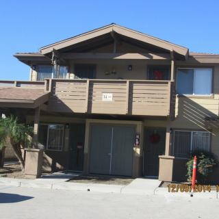 A two-story residential building with a balcony and a palm tree in front.