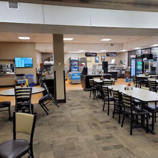 A spacious dining area featuring several tables and chairs, along with vending machines in the background.