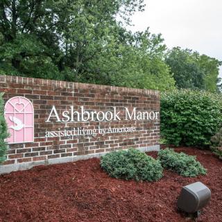 Entrance sign for Ashbrook Manor surrounded by landscaping and greenery.