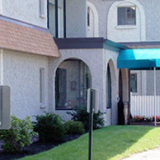 An exterior view of a building featuring arched windows, a green awning, and well-maintained landscaping.
