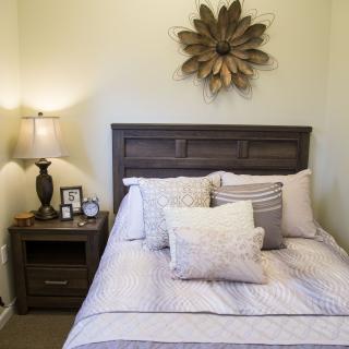 A cozy bedroom with decorative pillows, a bedside lamp, and wall art above the headboard.