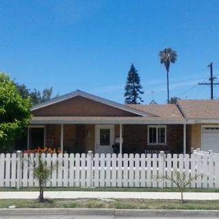 A suburban house with a white picket fence and palm trees under a clear blue sky.