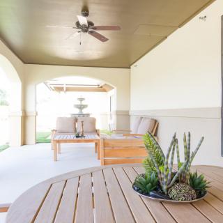 A modern outdoor patio featuring comfortable seating, a ceiling fan, and decorative plants.