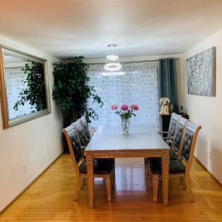 A well-lit dining room featuring a table set with chairs, adorned with flowers, surrounded by elegant decor and greenery.