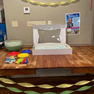 A festive setup featuring a cake box at the center, surrounded by colorful plates and party decorations.