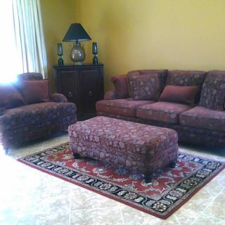 A cozy living room with a matching sofa set, ottoman, and rug.
