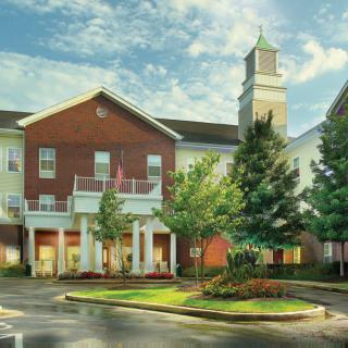 A residential building with a brick facade and a clock tower, surrounded by trees.