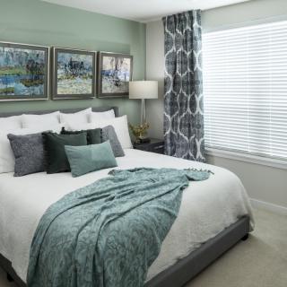 A modern bedroom featuring a neatly made bed with green accents, decorative pillows, and elegant wall art.