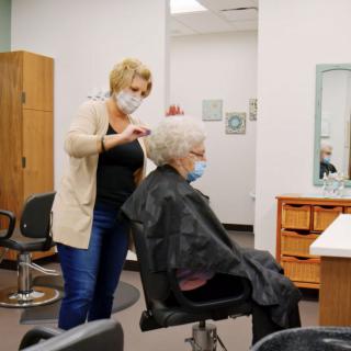 A hairstylist wearing a mask provides a haircut to an elderly client in a salon.