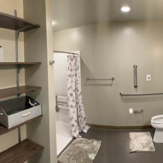 A modern bathroom with a shower, toilet, and shelves featuring grab bars for accessibility.