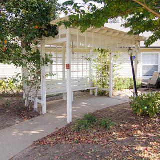 A cozy outdoor pergola with a bench offers a peaceful garden retreat along a paved pathway.