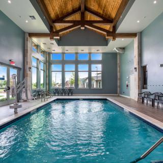 A modern indoor swimming pool with large windows and a wooden ceiling, allowing ample natural light.