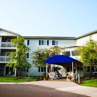 A three-story residential building with a blue awning over the entrance, surrounded by trees and landscaping.