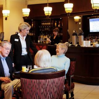 A relaxed social gathering in a bar setting where seniors engage in conversation while being served by waitstaff.