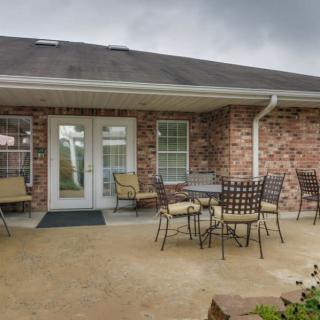 A well-furnished patio area with tables and chairs outside a brick house under a cloudy sky.