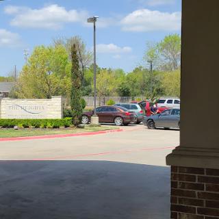 A view of a parking lot with several cars and green trees under a blue sky.