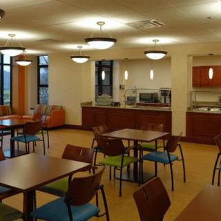 A modern cafeteria with tables and chairs, featuring warm lighting and a service counter.