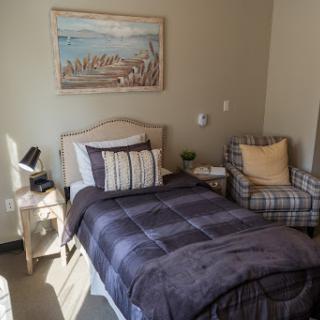 A cozy bedroom featuring a single bed, comfortable armchair, and framed artwork on the wall.