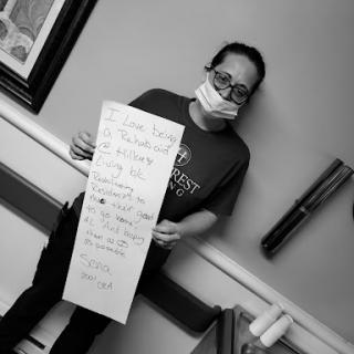 A person wearing a mask holds a sign in a hospital setting, conveying an important message.