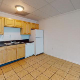 An unfurnished apartment kitchen with wooden cabinets, a refrigerator, and a tiled floor.