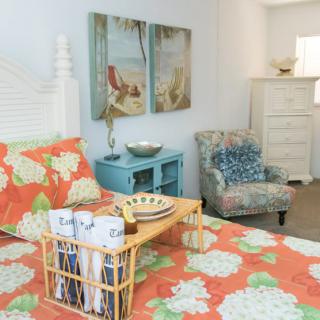 A cozy bedroom featuring floral bedding with a coastal theme, complemented by ocean-themed artwork and comfortable furniture.