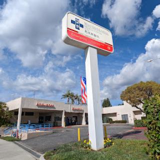 A storefront with a prominent sign and an American flag, set against a backdrop of blue skies and fluffy clouds.
