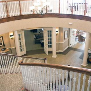 A view of a spacious interior lobby with a staircase, balcony, and classical columns.