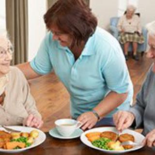A caregiver assisting elderly individuals during mealtime in a nursing home.