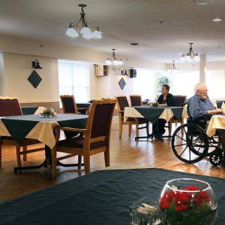 A quiet dining area in a nursing home with tables set for meals, featuring an elderly person in a wheelchair.