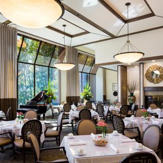 An elegant restaurant interior with neatly arranged tables, chandeliers, and a grand piano.