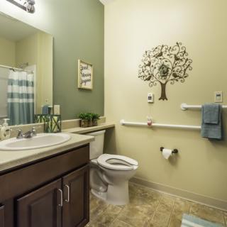 A cozy bathroom with decorative tree wall art, featuring a sink, toilet, and neatly arranged towels.