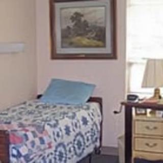 A cozy bedroom with a bed covered by a quilt, a bedside table with a lamp, and a framed painting on the wall.